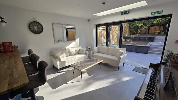A modern living room with a piano, two white sofas, a coffee table, and a large window providing a view of the outside.