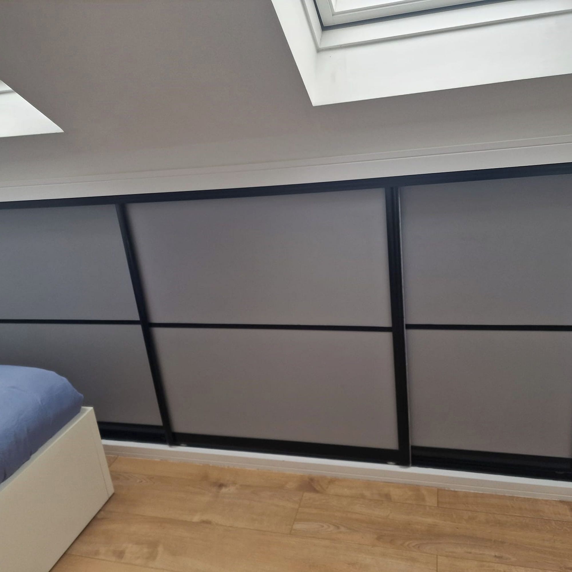 Un dormitorio con cabecera de listones, tragaluz y suelo de madera.