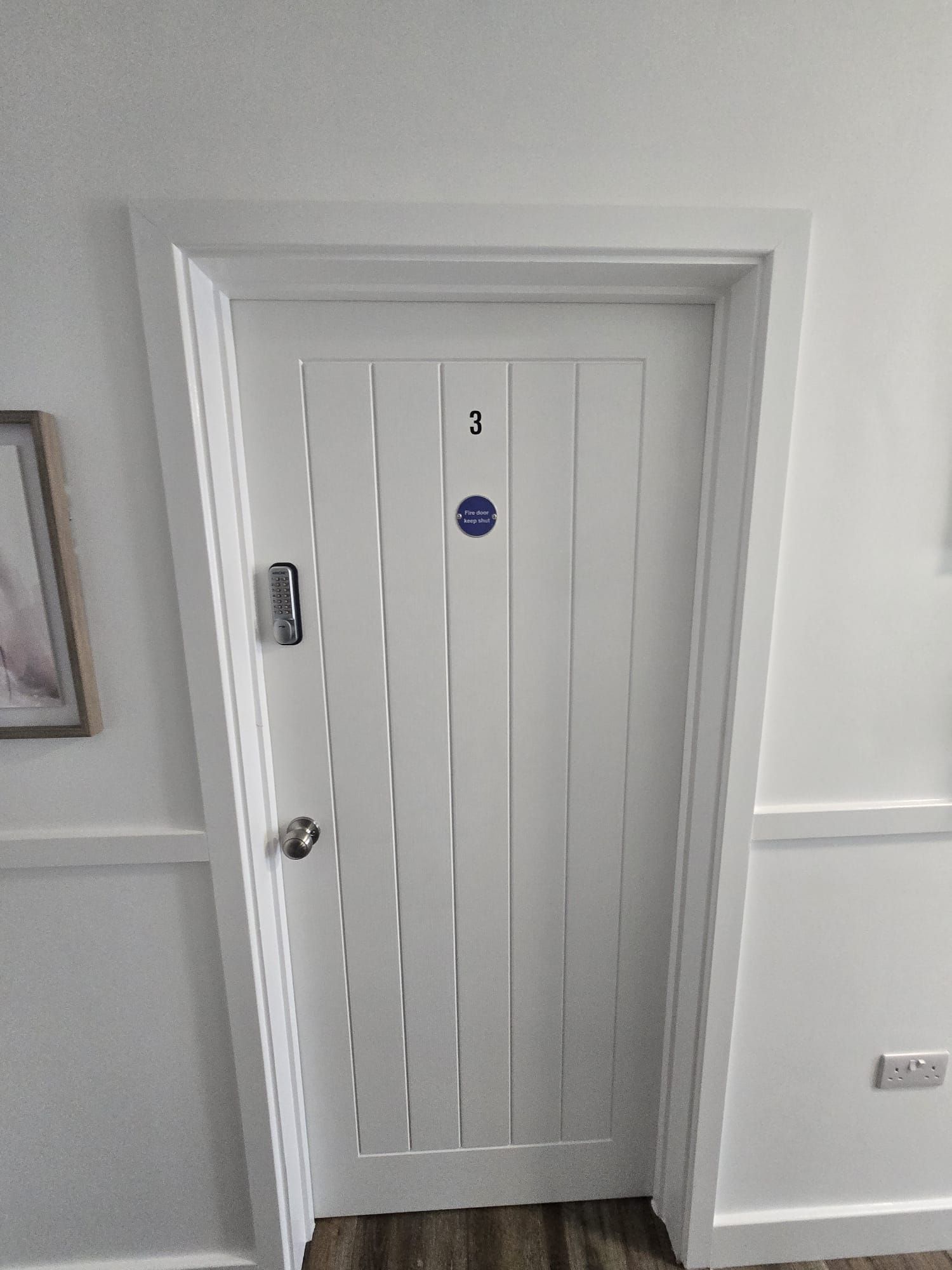 A white door with a number 3 sign, a keypad lock, and a fire door keep shut sign.