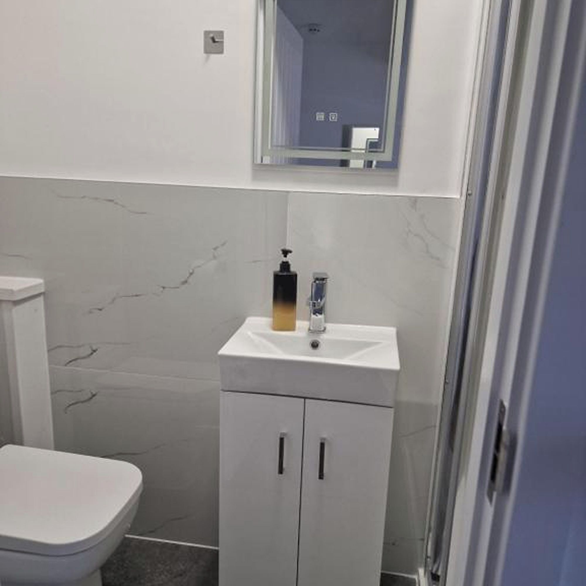 A small bathroom with a white toilet, a sink with a soap dispenser, and a mirror above the sink.