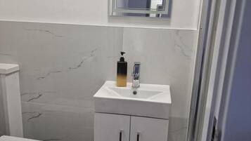 Un baño pequeño con inodoro blanco, lavamanos con dispensador de jabón y espejo sobre el lavamanos.