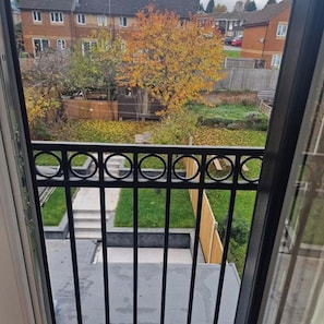 A view from a balcony with a black metal railing, a grassy yard, and a tree with autumn leaves. - Albion's House (Luton)