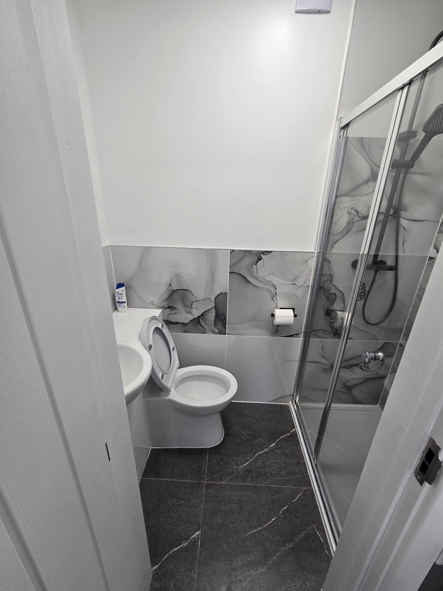 Une petite salle de bain comprenant des toilettes, un espace douche et un sol carrelé en marbre.