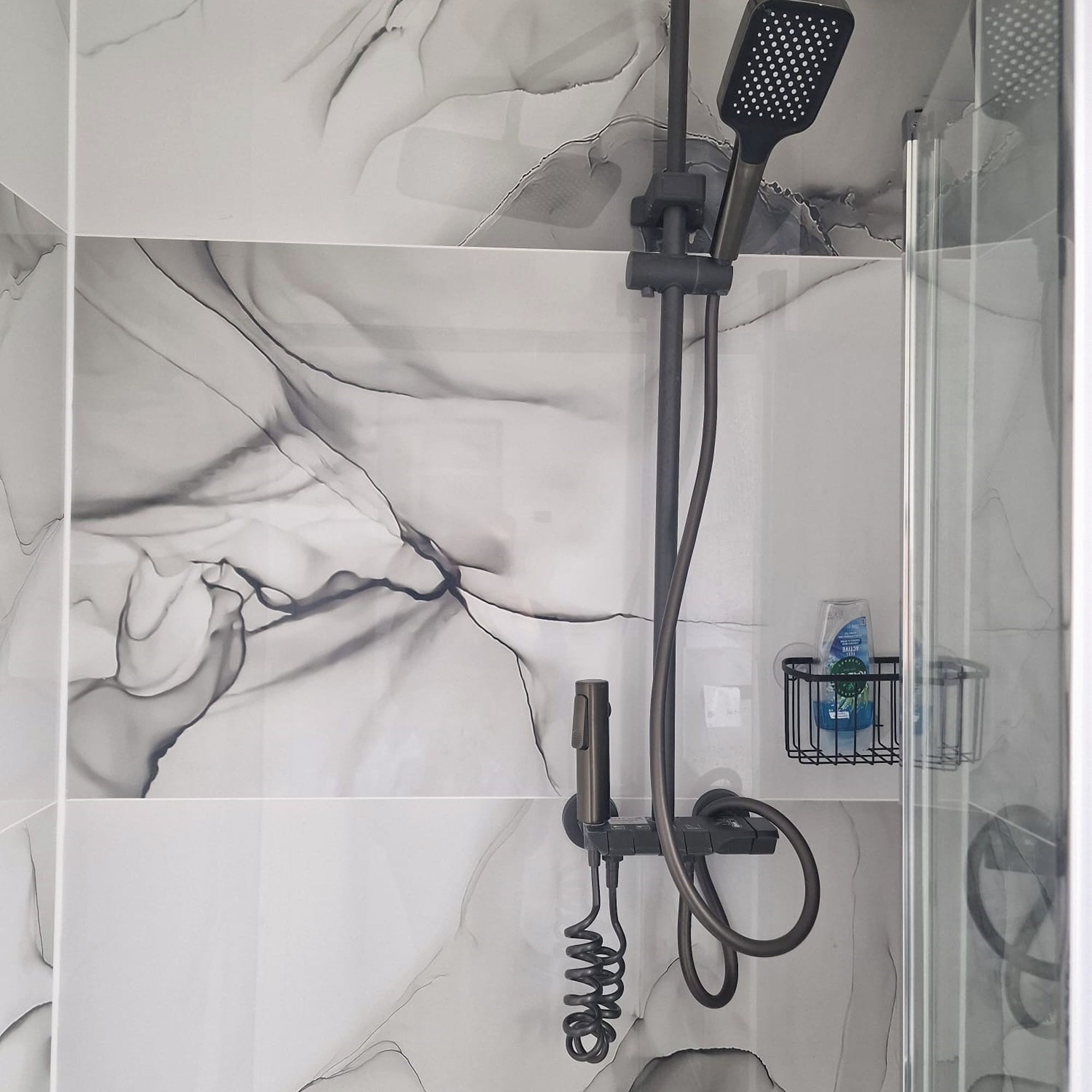 Un baño con ducha, cabezal de ducha de mano, masajeador de mano y mampara de vidrio.