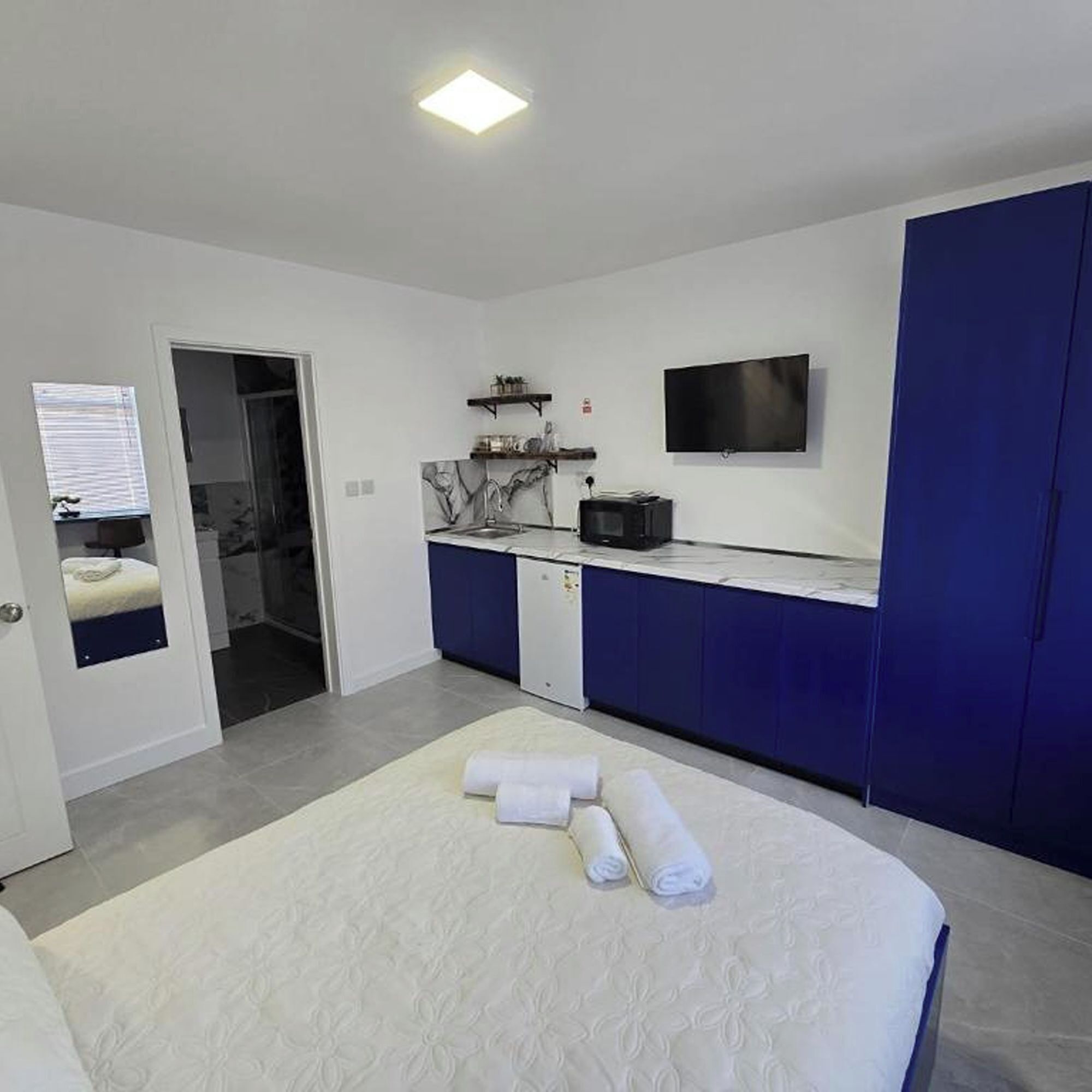 Ein modernes Schlafzimmer mit einem großen Bett, einem an der Wand montierten Fernseher und einer Küchenzeile mit blauen Schränken.