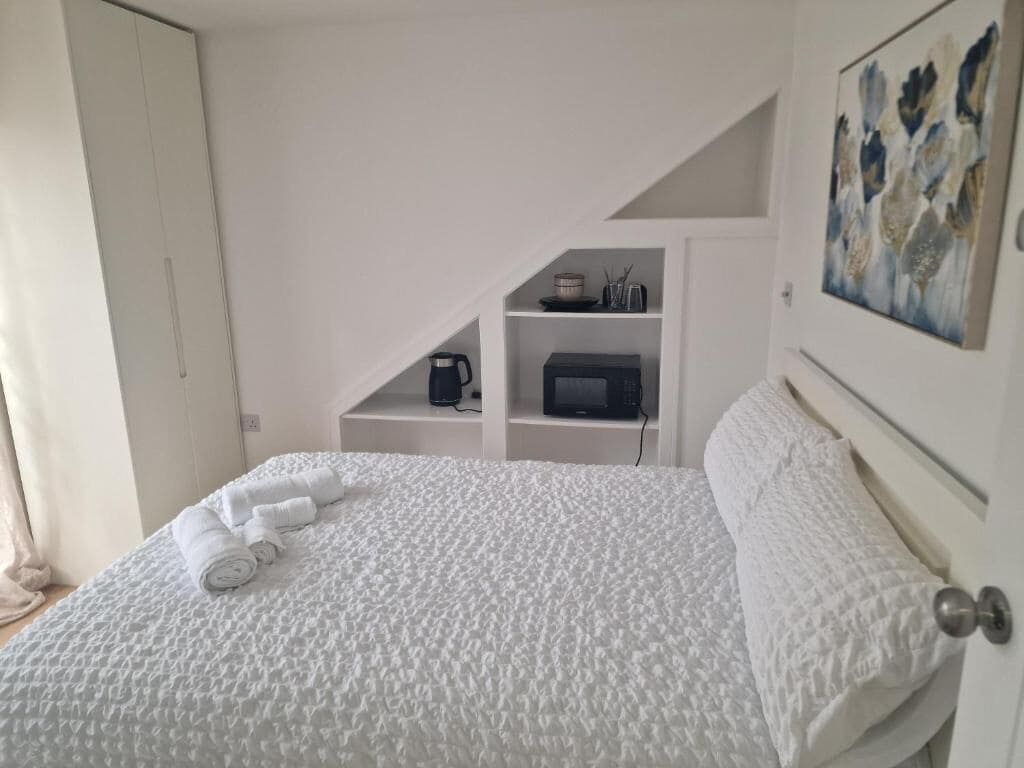 Une chambre à coucher avec un lit, une porte blanche, un tableau et une étagère sur laquelle se trouvent une bouilloire et un four à micro-ondes.