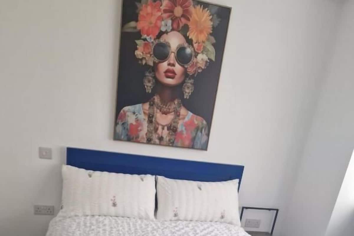 A neatly made bed with white linens and rolled towels, a blue headboard, and a floral artwork on the wall.
