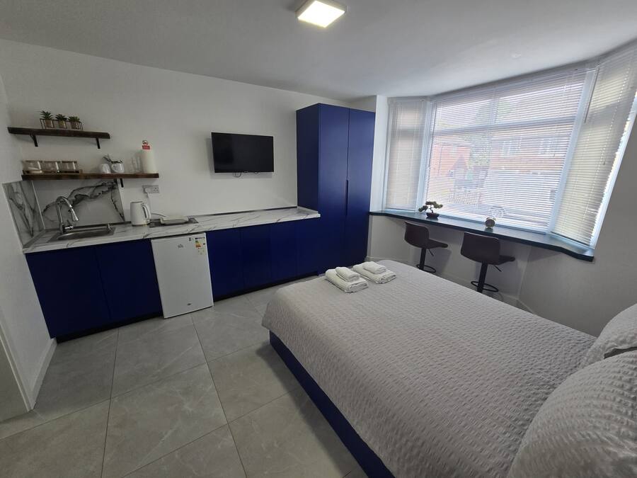 A bedroom with a bed, a desk, a television, and a window with blinds.