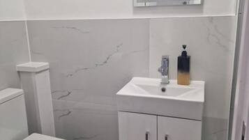 A small, modern bathroom with a white toilet, a white sink with a soap dispenser, and a mirror above the sink.