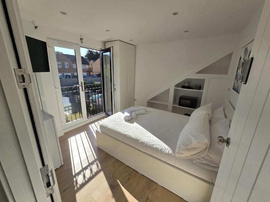 Ein Schlafzimmer mit Bett, einer integrierten TV-Konsole und einem Balkon mit Blick auf Häuser.