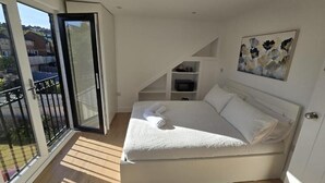 A bedroom with a bed, a painting, a sliding door, and a balcony.