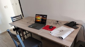 Una scrivania in legno con un laptop, un sottotavoliino rosso, auricolari, uno smartphone e un quaderno.