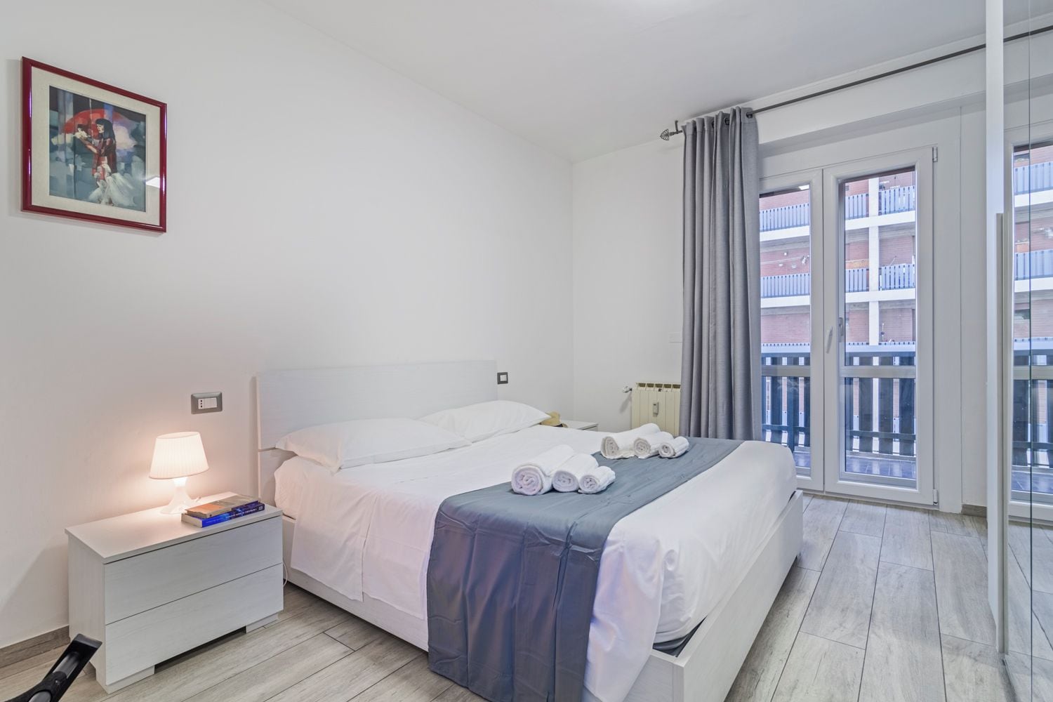 Une chambre d’hôtel avec un lit, une table de chevet, une lampe et une vue sur le balcon extérieur.