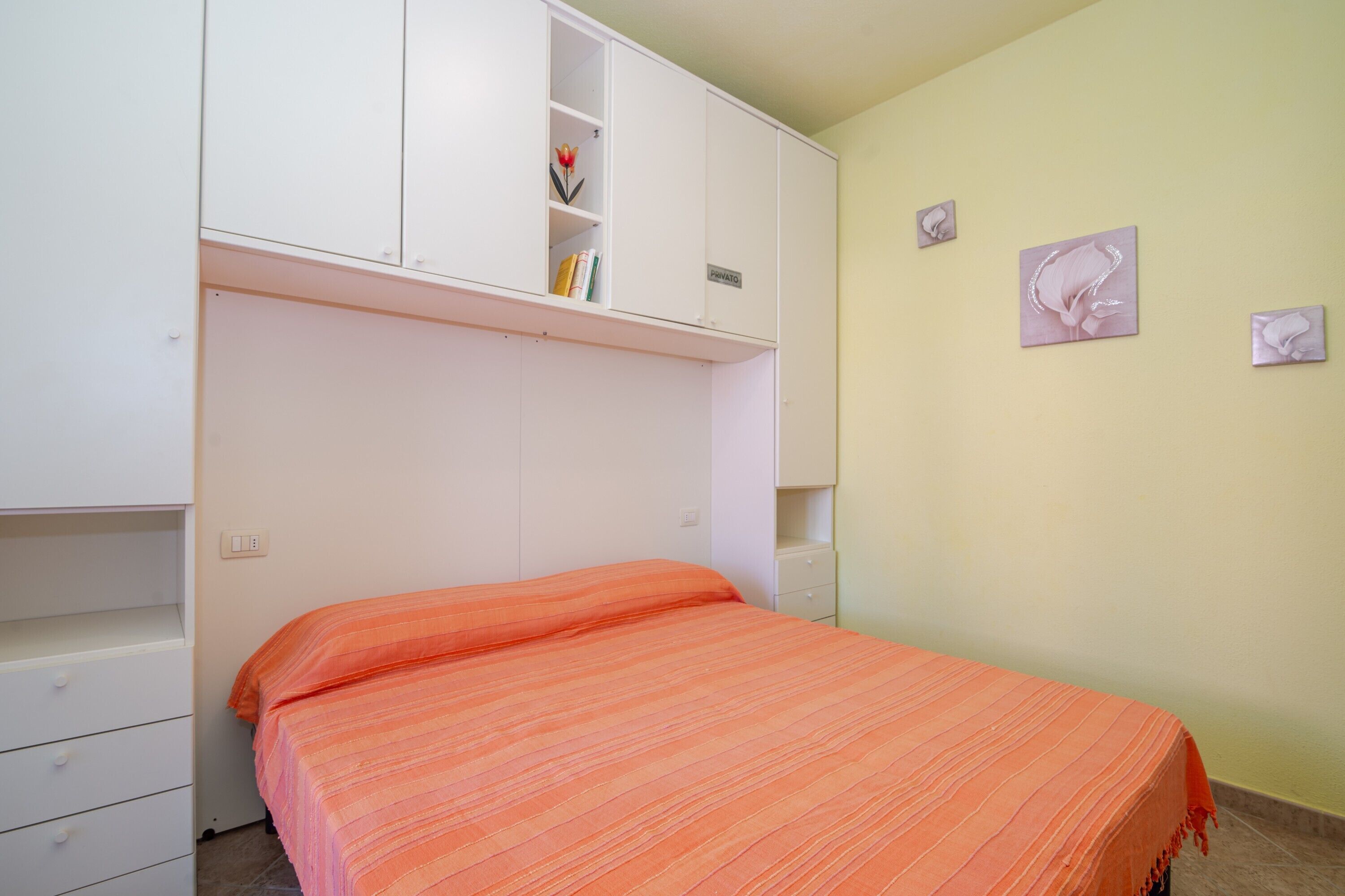 Une chambre à coucher avec un lit, une armoire et une étagère contenant des livres et une fleur.