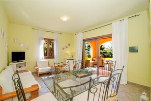 A living room with a glass-top table, chairs, a sofa, a television, and a view of a garden through an open door. - Cottage with Garden in the Center – Private Terrace, Private Garden, Air Conditioning (Suaredda-traversa)