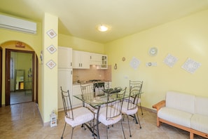 A dining area with a glass table and metal chairs, a kitchen with white cabinets, and a living area with a sofa.