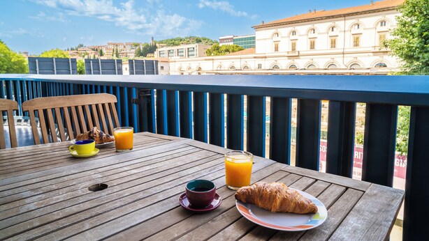 Et træbord med morgenmadsprodukter, heriblandt en croissant, et glas appelsinjuice og en kop kaffe.
