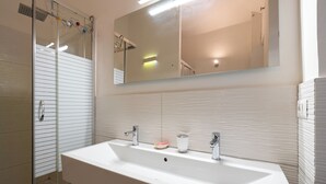 Ein modernes Badezimmer mit einem großen, weißen Waschbecken, einem Spiegel und einer Duschkabine aus Glas.