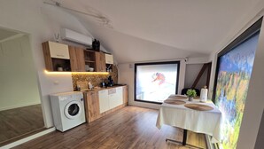 A compact kitchen with wooden cabinets, a washing machine, and a large window with a mountain view.
