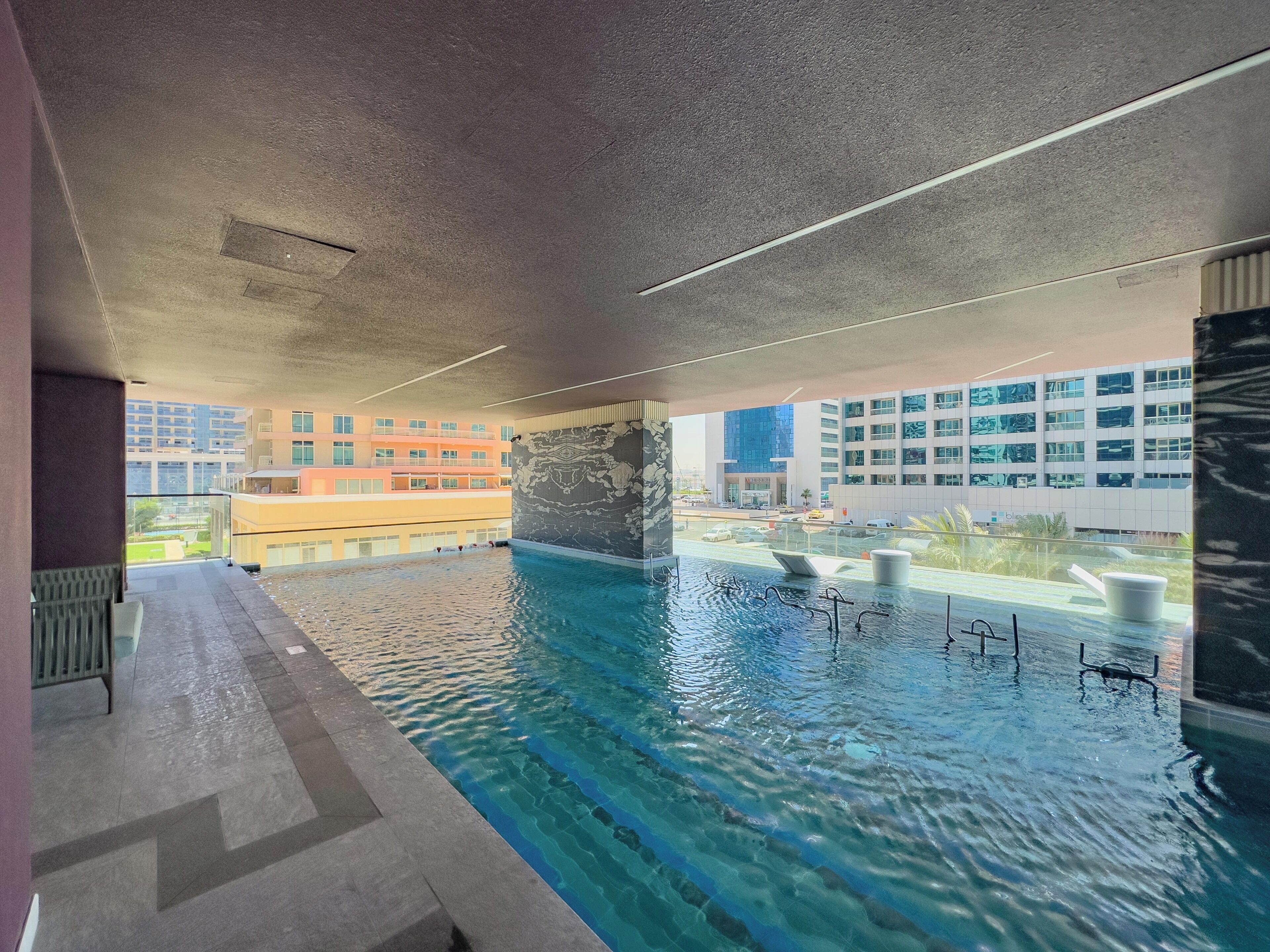 An indoor swimming pool with clear water, a view of the cityscape, and a modern architectural design.
