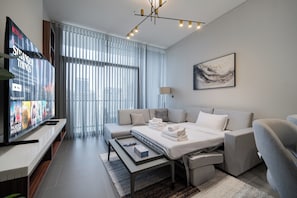 A modern hotel room with a large flat-screen TV, a sofa bed, a bedside table, and a window with sheer curtains. - SettlerHomes - Chic JLT 29th Floor - Near Panoramic Lake (Dubai)