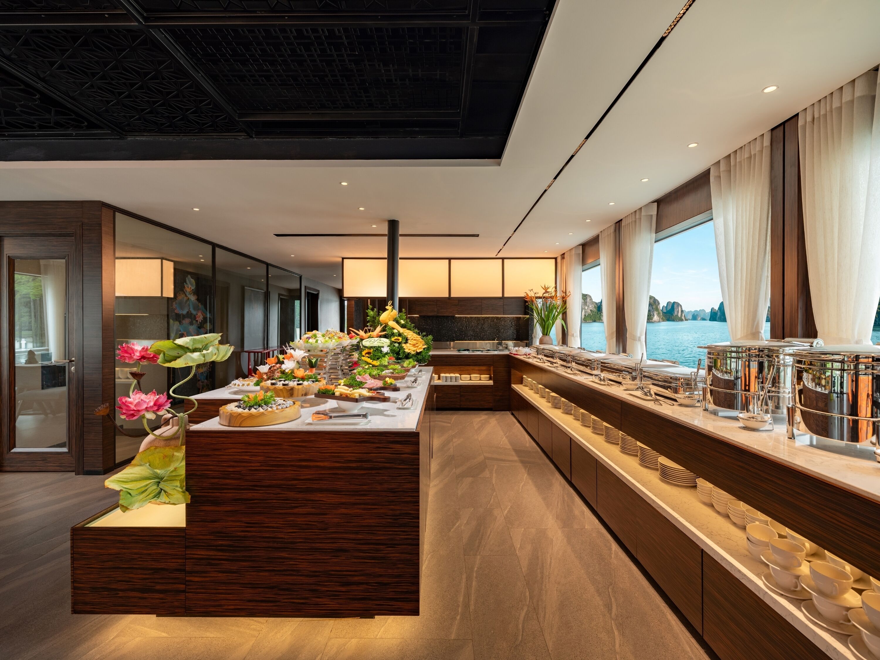 Cocina moderna con una isla central, equipada con diversos alimentos y utensilios, y vistas al mar a través de amplios ventanales.
