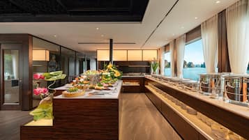 Cocina moderna con una isla central, equipada con diversos alimentos y utensilios, y vistas al mar a través de amplios ventanales.