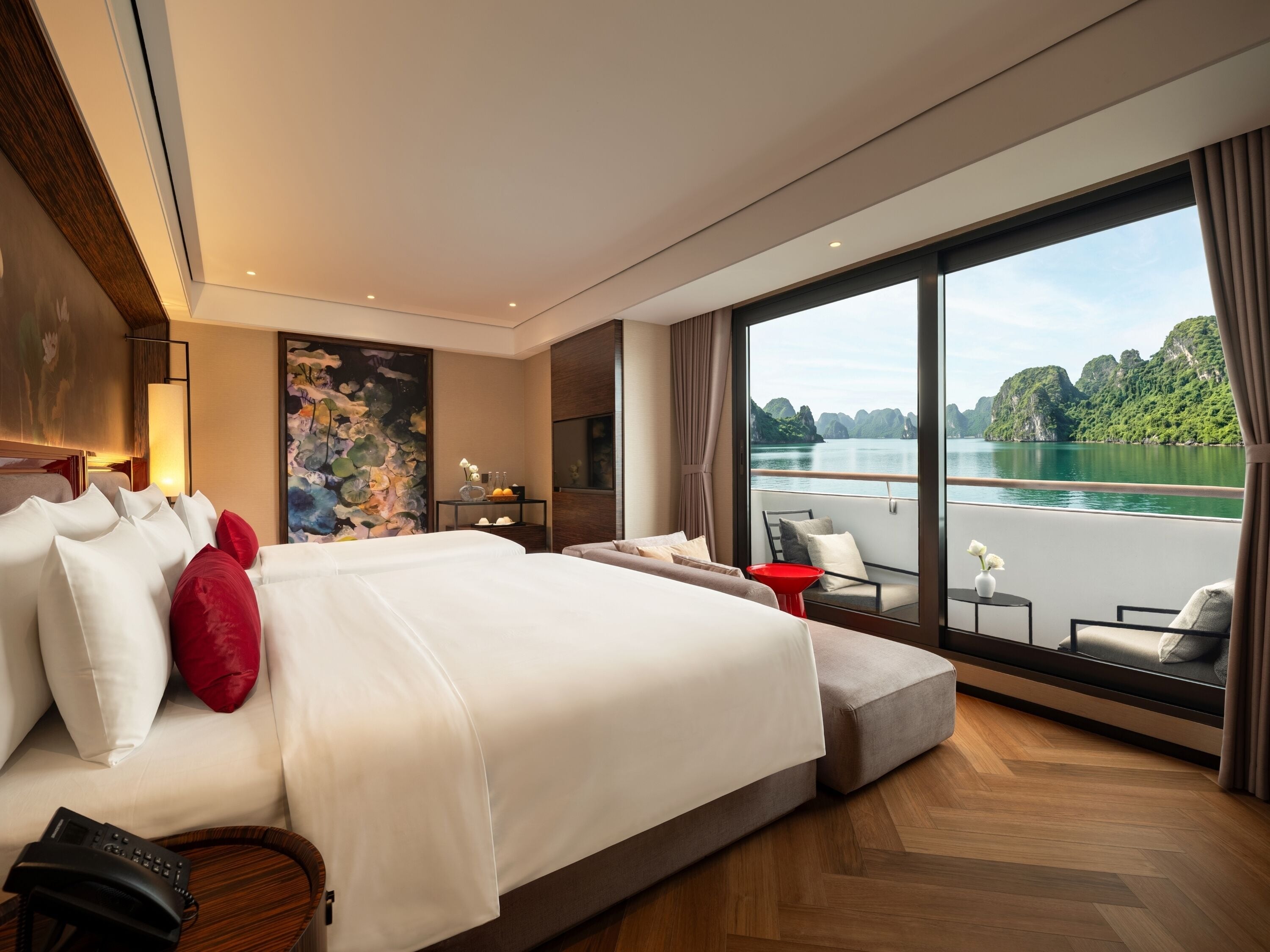 A modern hotel room with a large bed, a balcony with a view of a lake, and a painting on the wall.