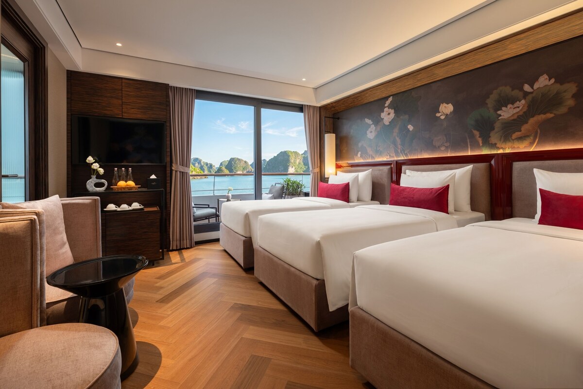 Una habitación de hotel con un ventanal grande, una cama, un sofá, un televisor y una mesita.