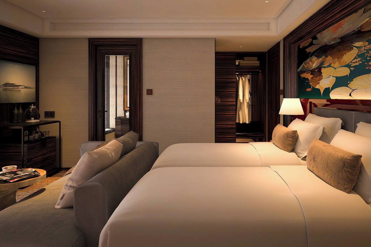 A hotel room with a large bed, a seating area with a coffee table, a desk with a lamp, and a large floral artwork on the wall.