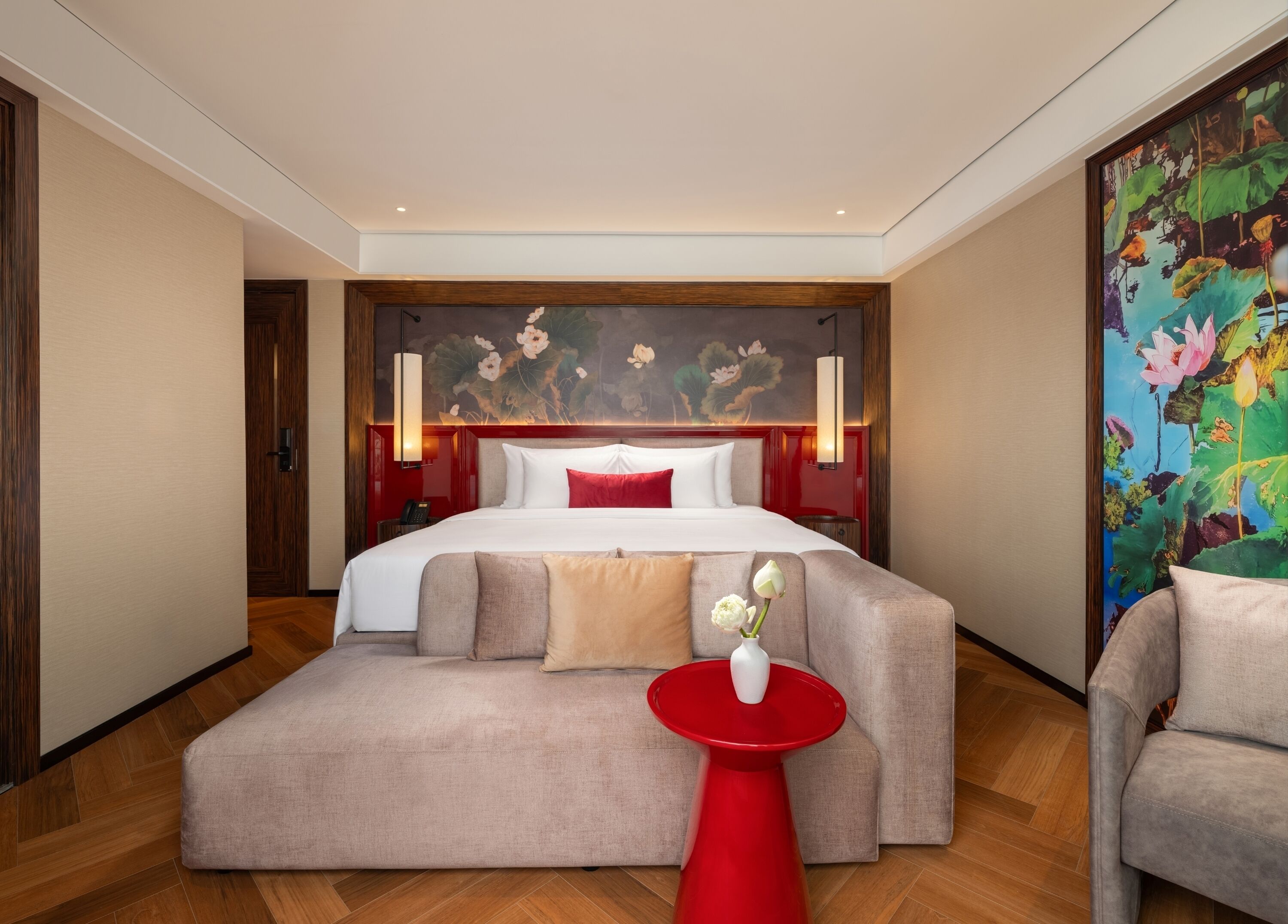 A hotel room with a bed, a red side table, a sofa, and a painting on the wall.