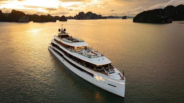 A large, multi-deck yacht with outdoor seating areas and a helipad, sailing in a calm body of water with distant landforms. - La SEN of the Bay Cruises  (Tuan Chau)