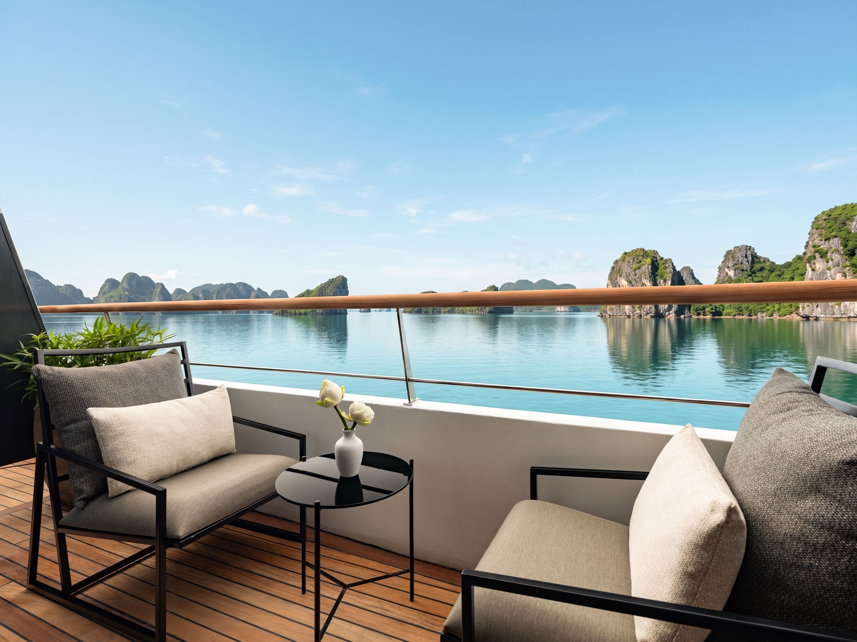 A deck with two chairs and a small table, overlooking a calm body of water and rocky landscape.