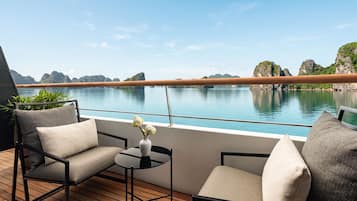 A deck with two chairs and a small table, overlooking a calm body of water and rocky landscape.