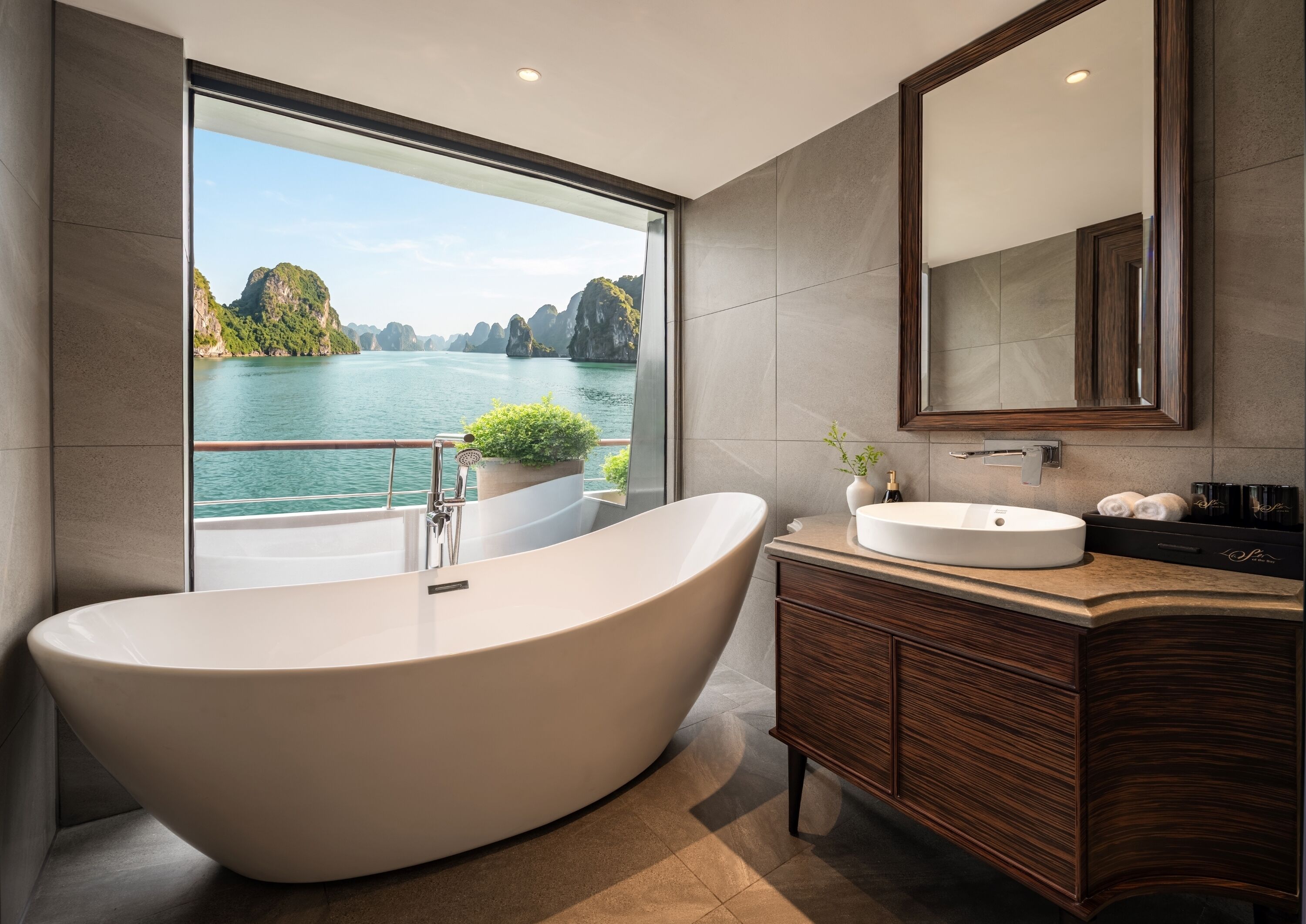 Ein modernes Badezimmer mit einer freistehenden Badewanne, einem großen Spiegel und Blick auf ein Gewässer mit Bergen.