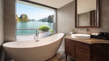 Ein modernes Badezimmer mit einer freistehenden Badewanne, einem großen Spiegel und Blick auf ein Gewässer mit Bergen.