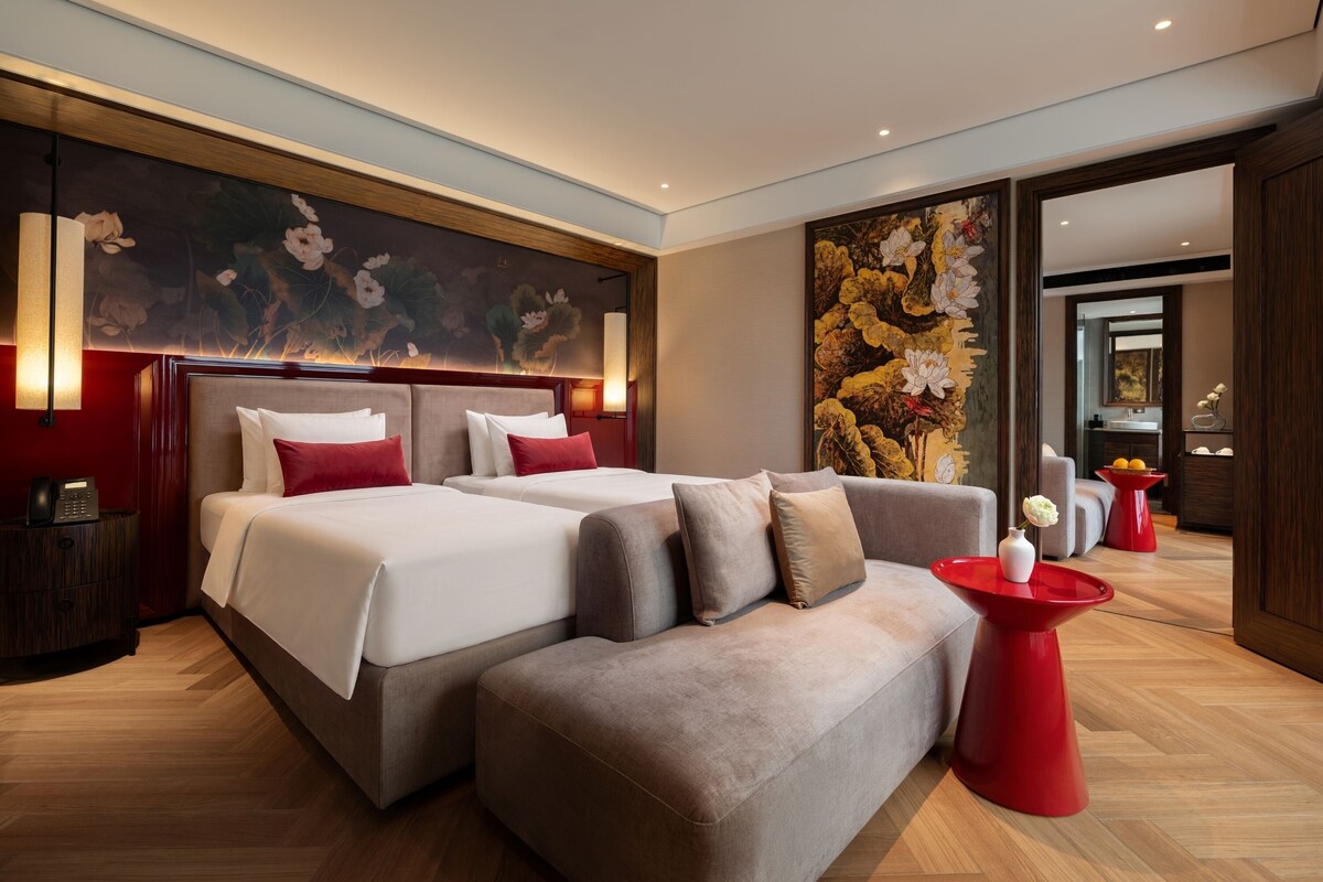 Una habitación de hotel moderna con una cama grande, un sofá y una mesita de centro roja.