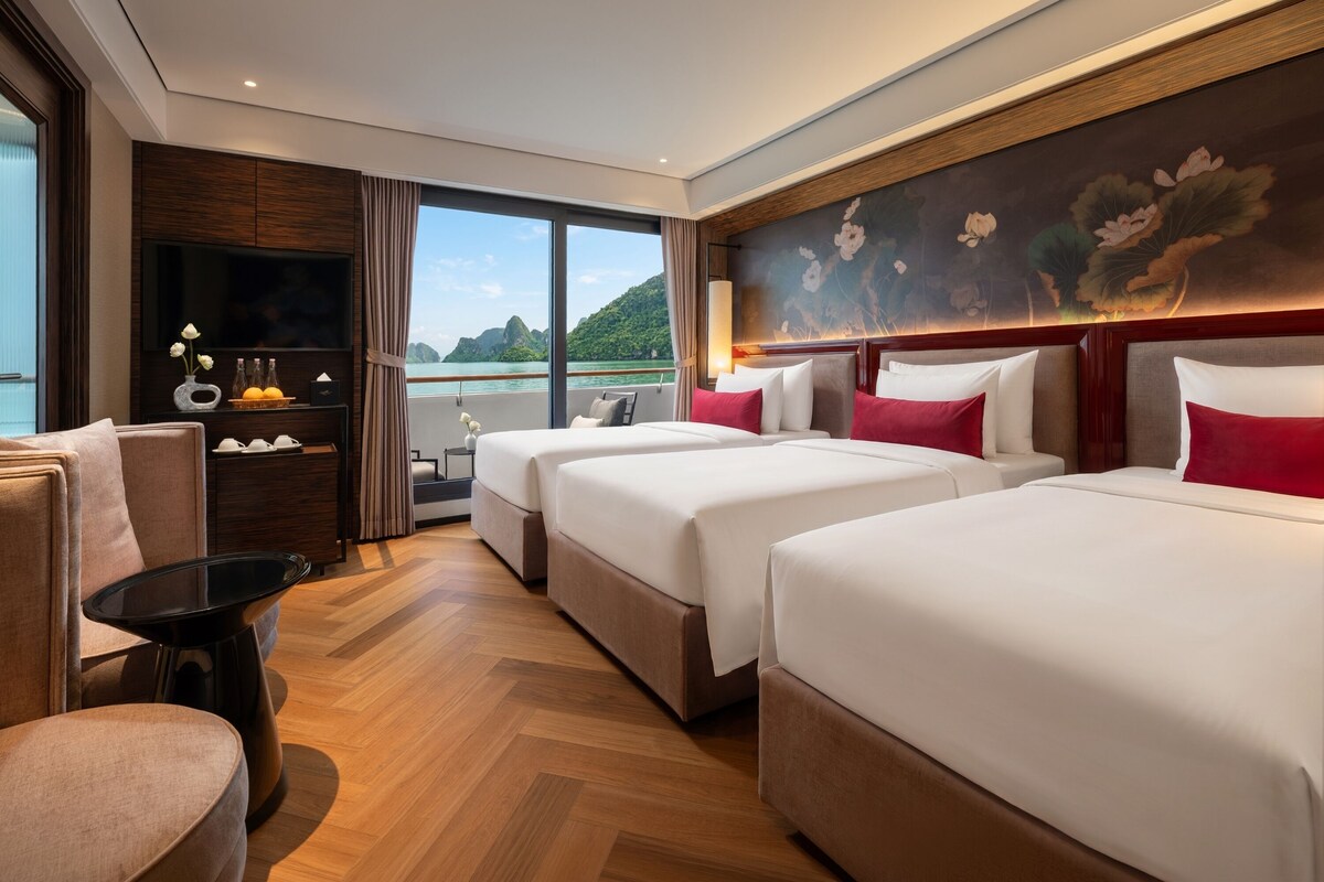 Habitación de hotel con dos camas, zona de estar, televisor y vista al mar.
