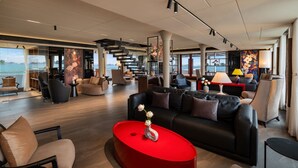 A spacious lounge area with a modern design, featuring a red coffee table, comfortable seating, and large windows offering a view of the sea. - La SEN of the Bay Cruises  (Tuan Chau)