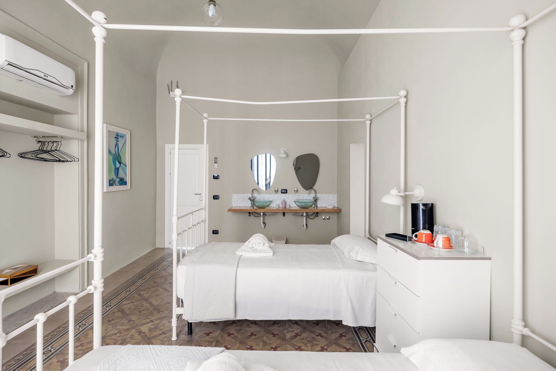 A bedroom with a four-poster bed, a bedside table with a lamp, a mirror, and a shelf with toiletries.