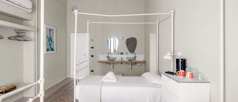 A bedroom with a four-poster bed, a bedside table with a lamp, a mirror, and a shelf with toiletries.