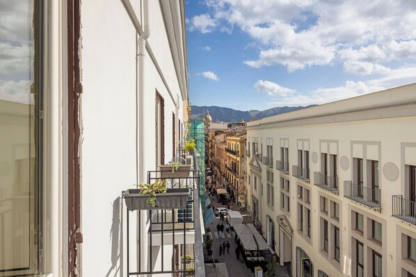 A narrow street with buildings on either side, a clear sky, and mountains in the distance.