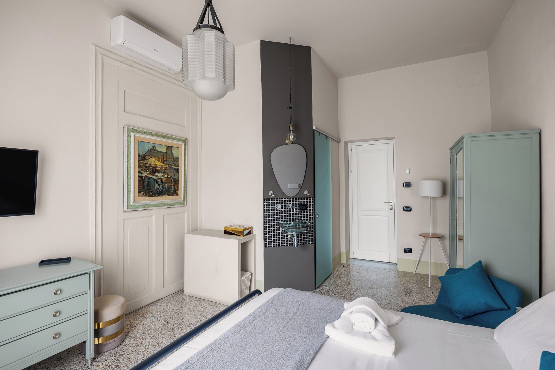 Habitación de hotel con cama, escritorio, armario, espejo, un cuadro y televisor.