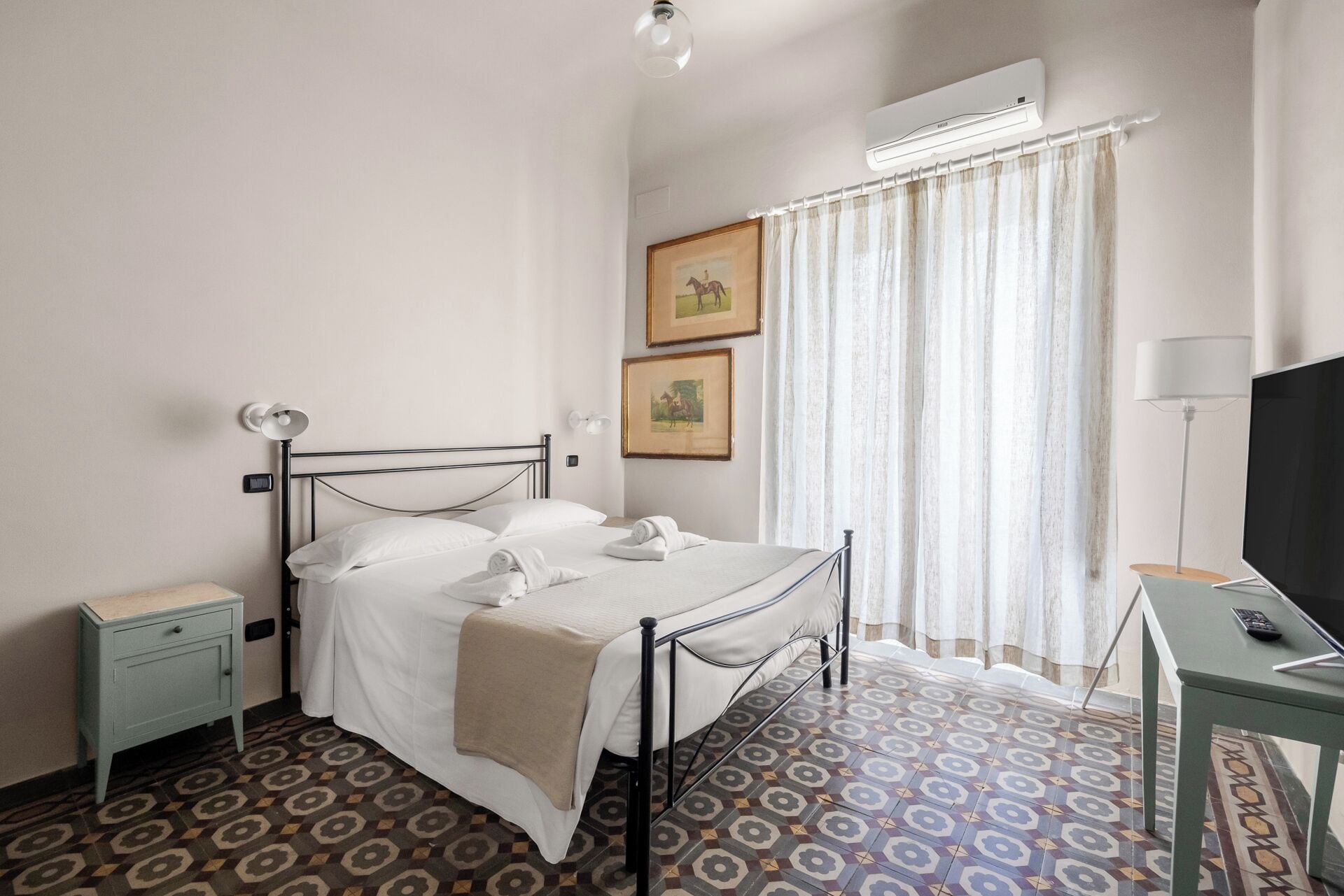 A hotel room with a bed, a desk, a TV, and an air conditioning unit.