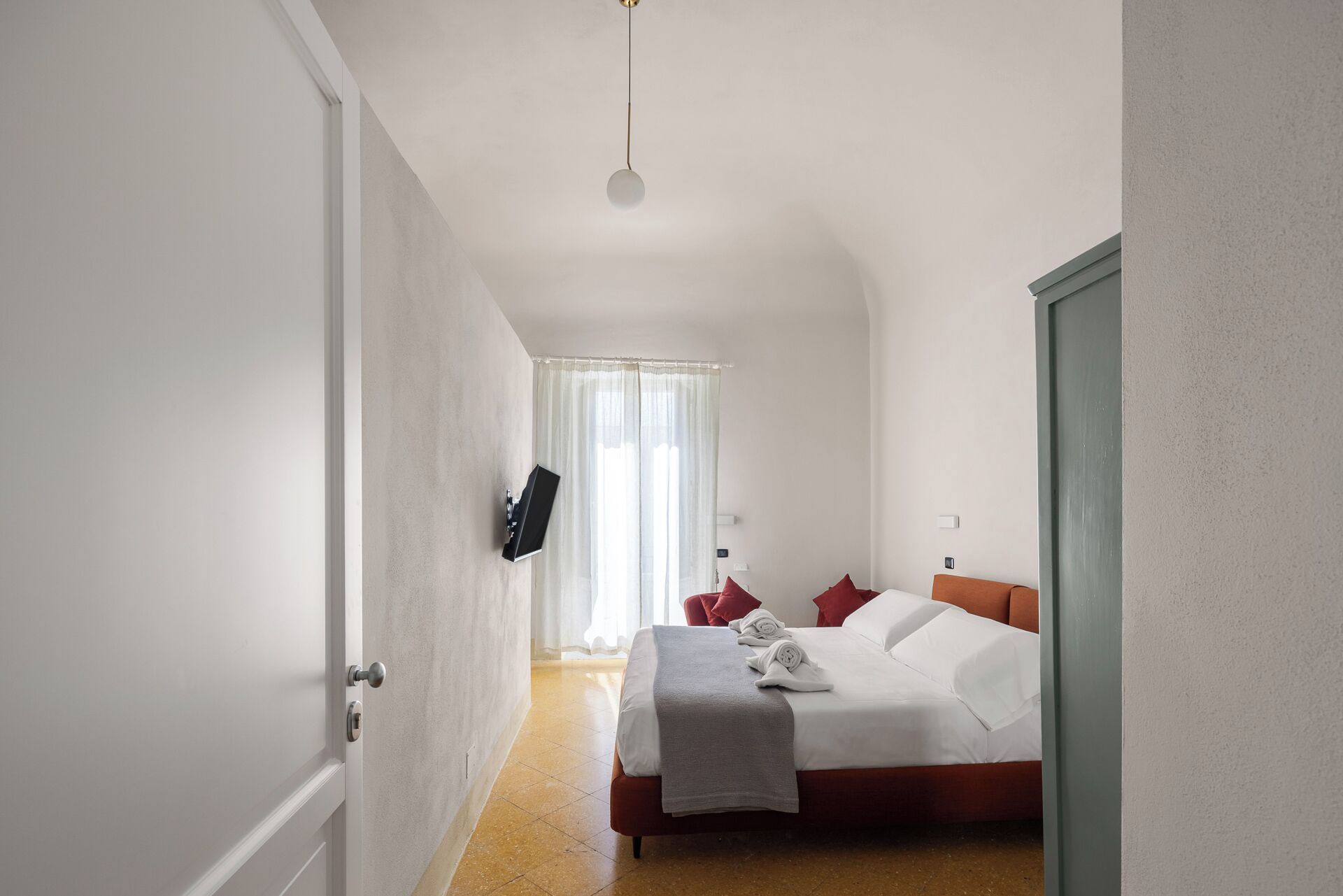 A bedroom with a bed, a TV mounted on the wall, and a door leading to another room.