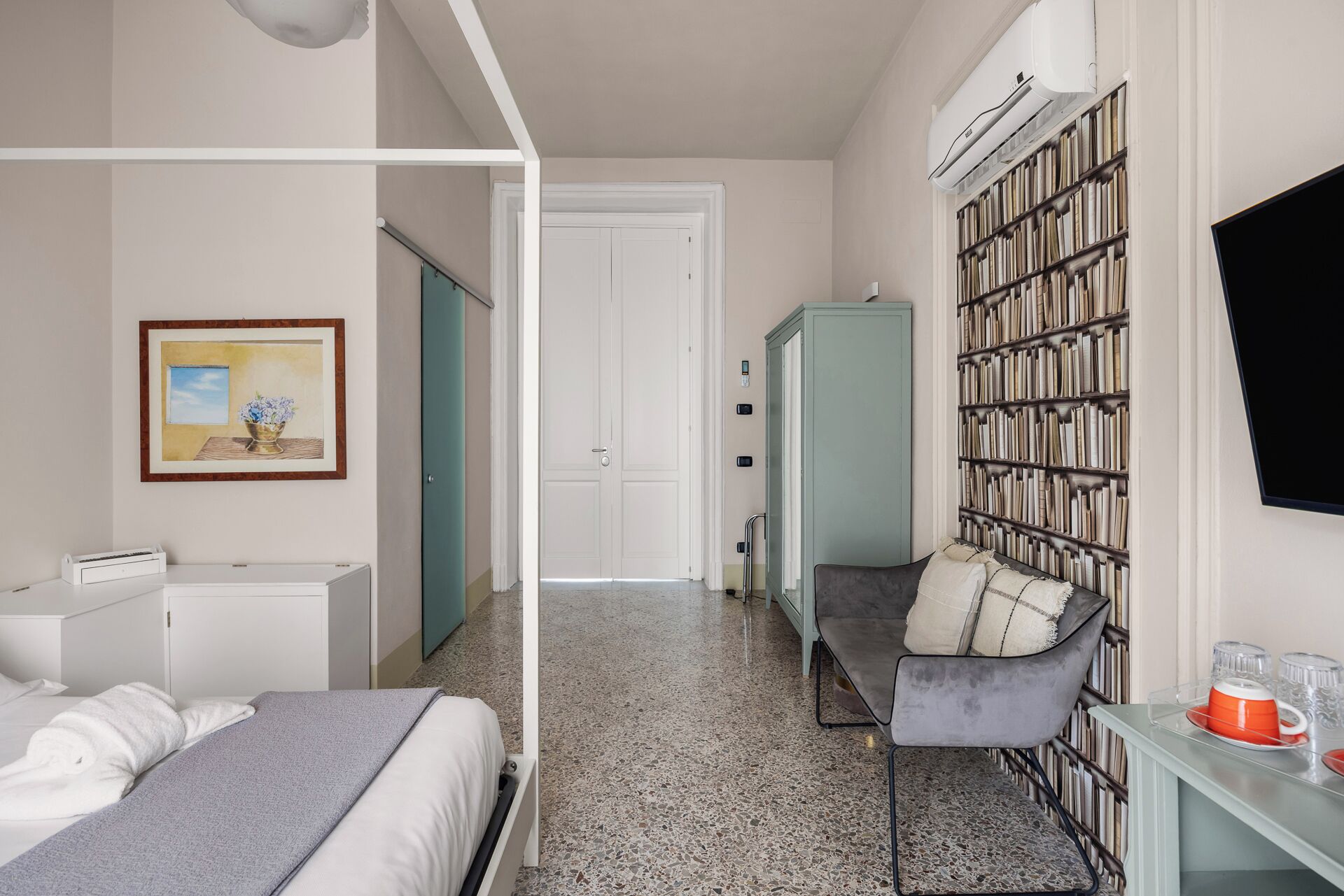 Un dormitorio con cama, escritorio, estantería y puerta que da a otra habitación.