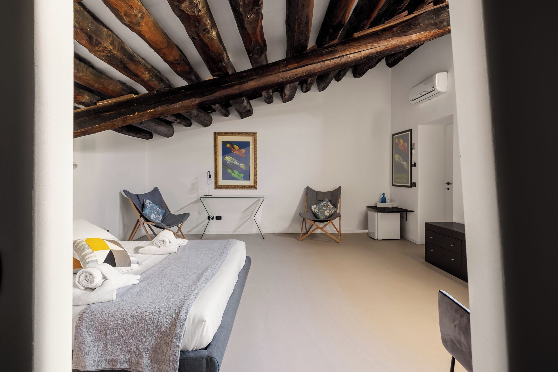 Una camera da letto con un letto, due poltrone, un tavolino, un condizionatore d'aria e opere d'arte alle pareti.