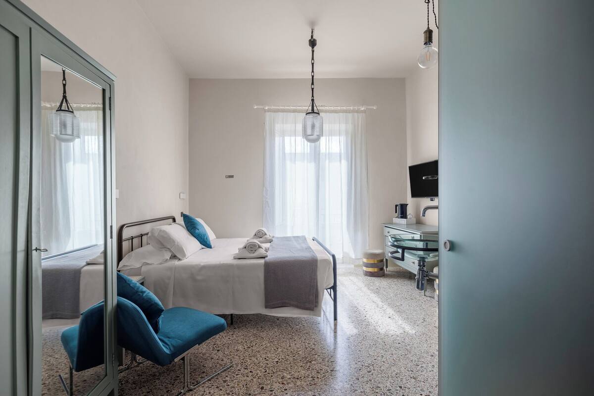 A hotel room with a bed, a chair, a desk, a television, and a mirror.