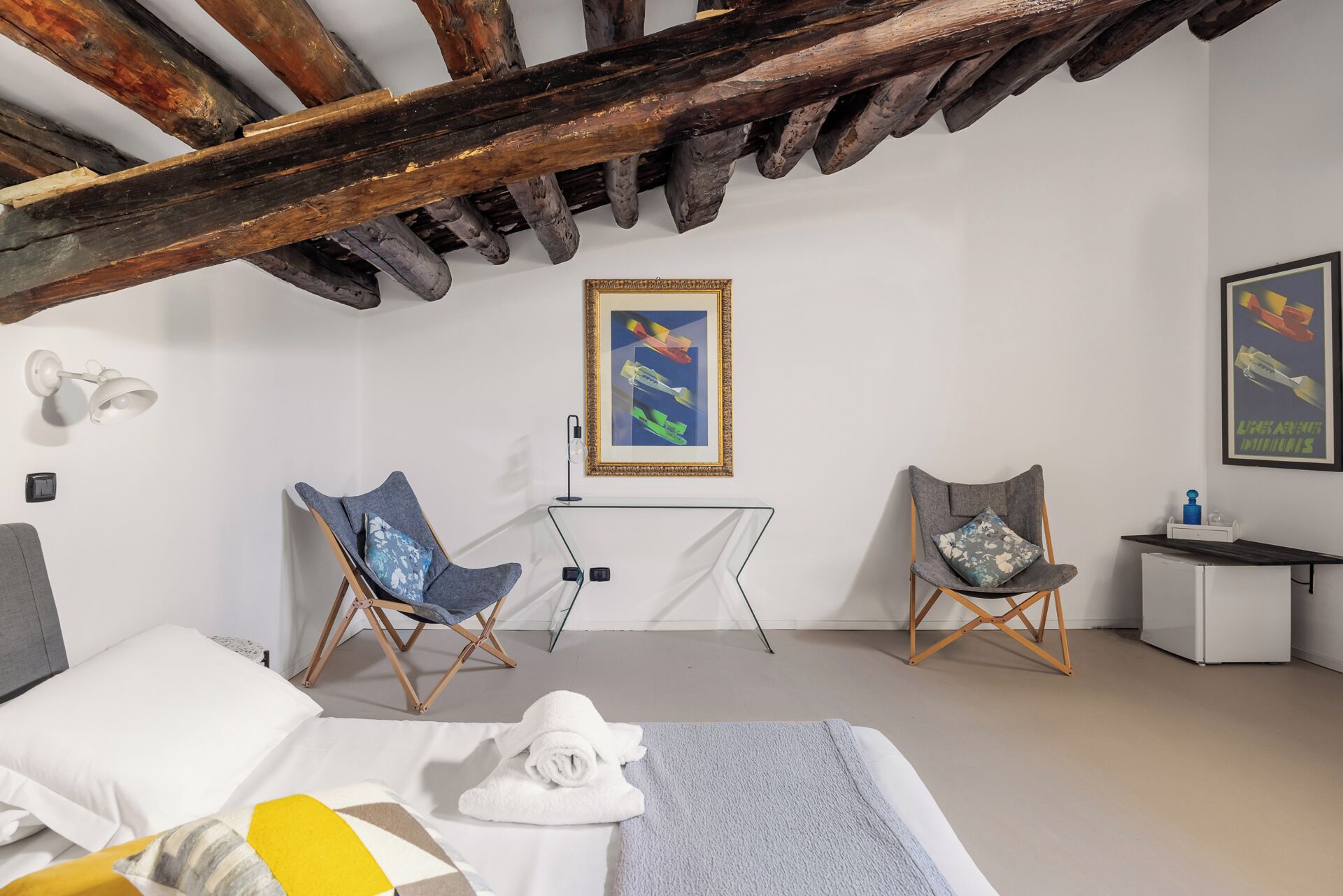 A bedroom with a bed, two armchairs, a small table, and a framed picture on the wall.