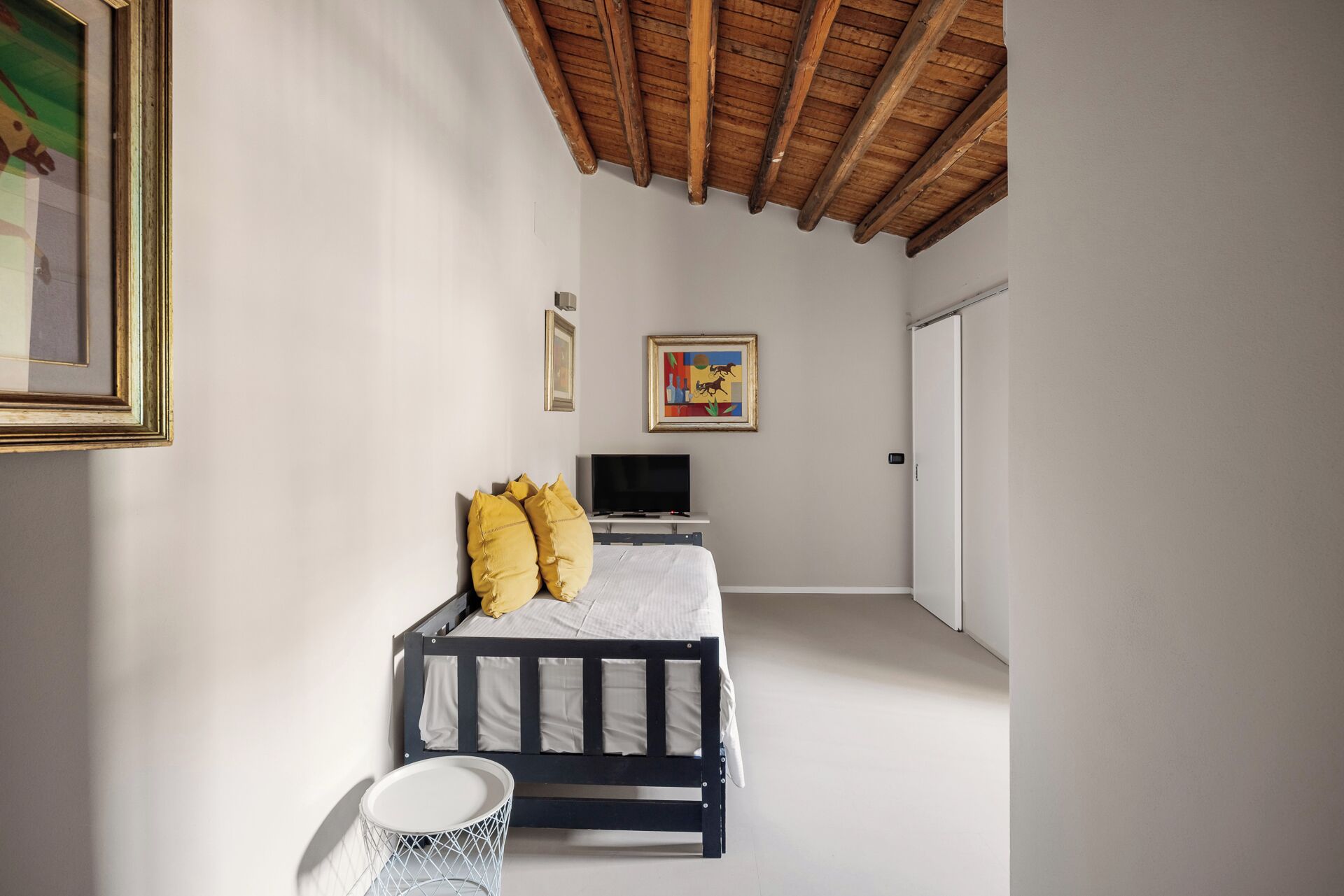 Un dormitorio con cama, televisión, cuadro y puerta.